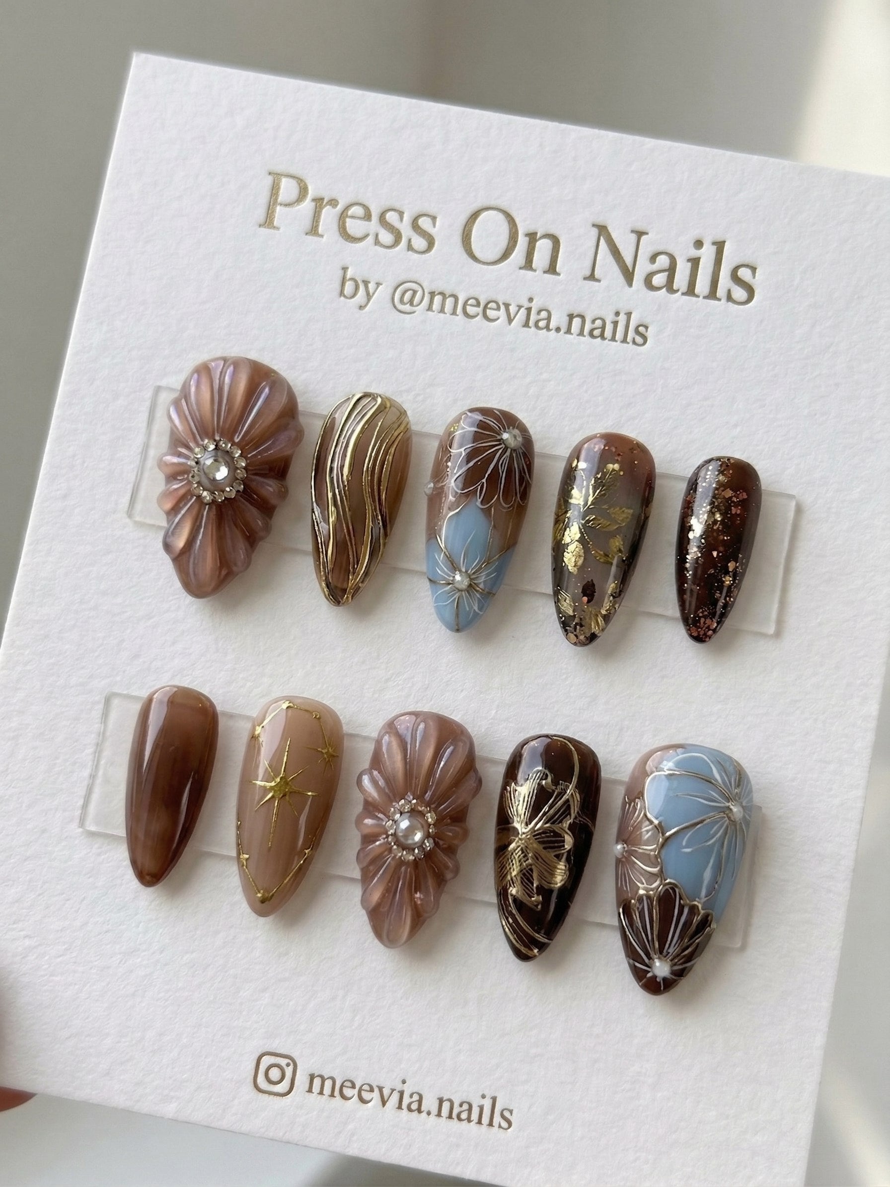 Almond-shaped brown and blue press-on nail set with 3D floral textures and gold art