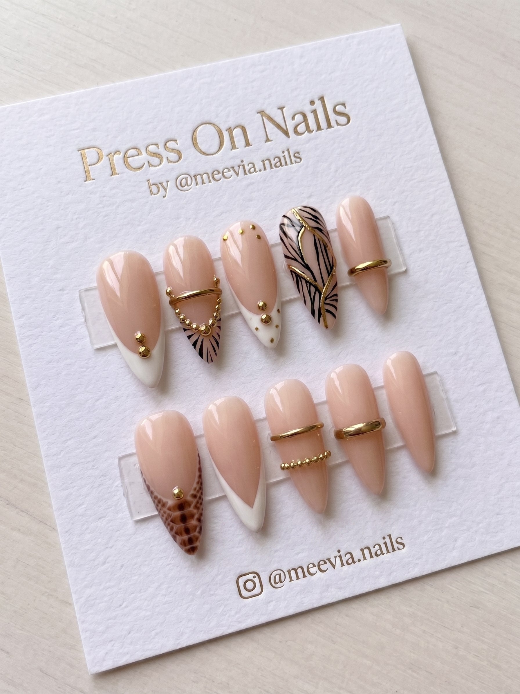 Almond-shaped nude French tip press-on nails with gold ring and bead embellishments