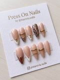 Almond-shaped nude press-on nails with animal print and 3D gold accents.