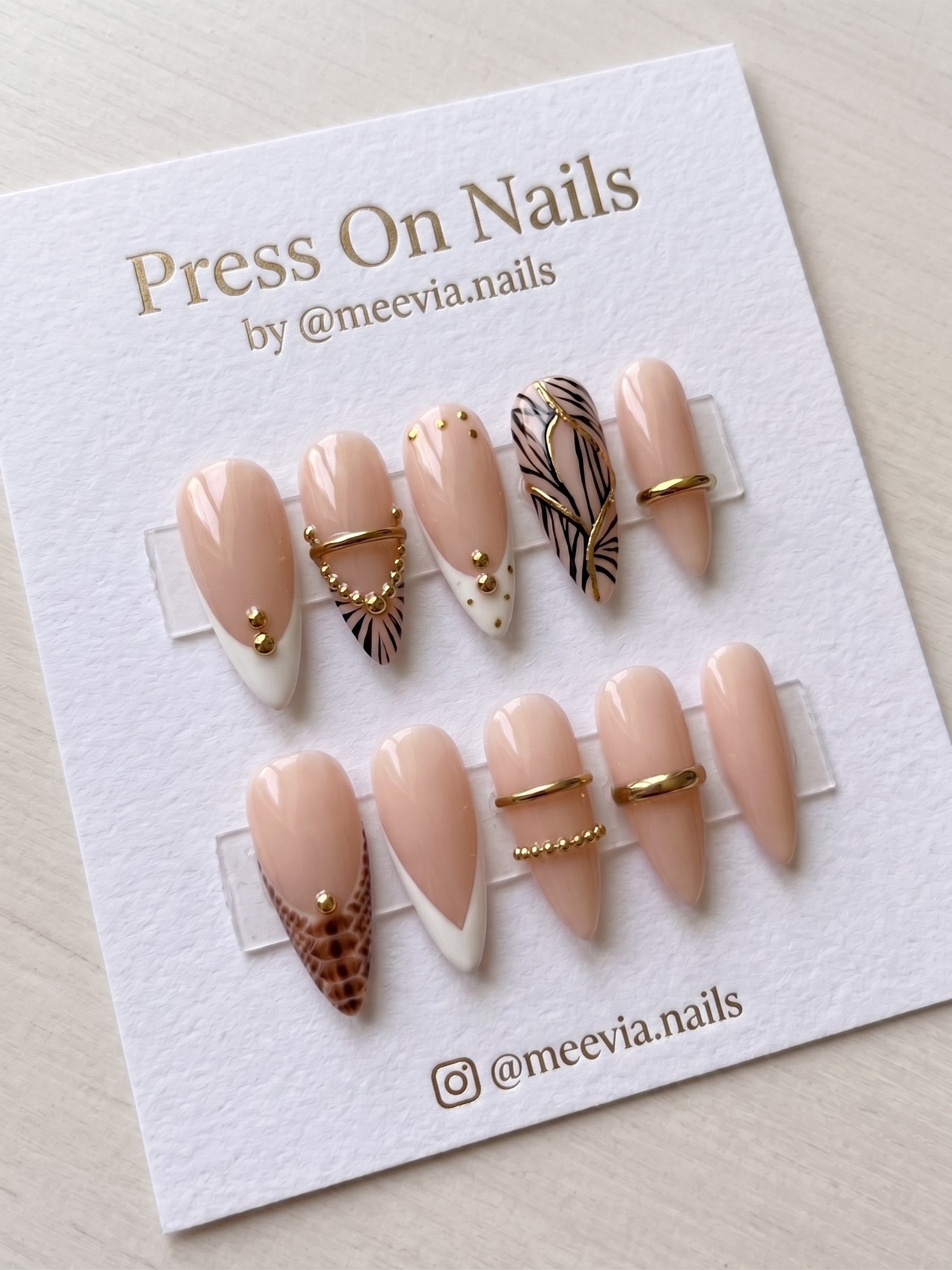 Almond-shaped nude press-on nails with animal print and 3D gold accents.