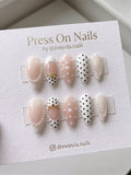 Almond-shaped press-on nails featuring white and nude colors with black polka dots, pearl borders, and gold bead accents as a complete nail set.