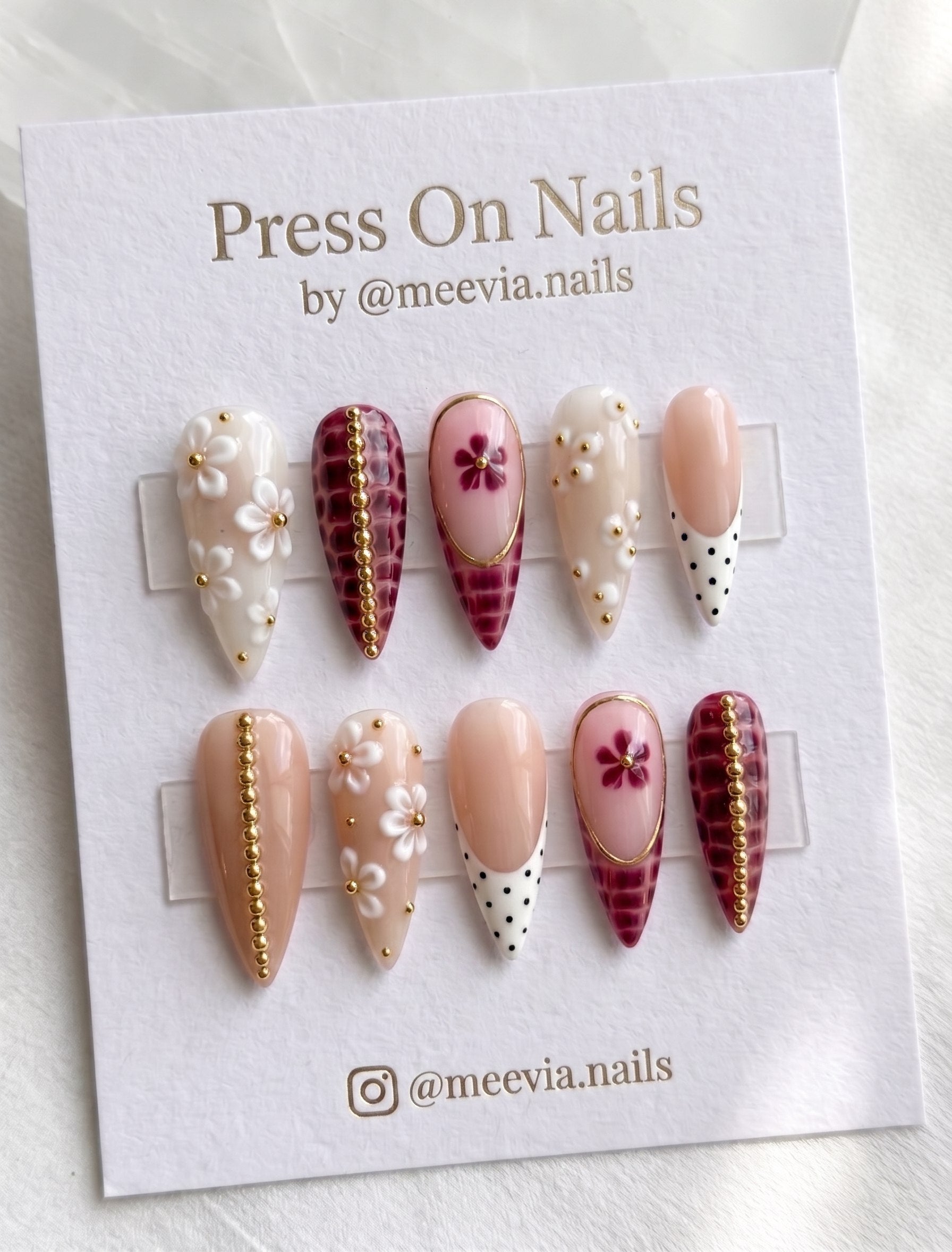 Stiletto-shaped burgundy and nude press-on nail set with 3D white flowers, gold beads, and polka dot French tips