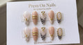 Almond-shaped nude and milky white press-on nails with black zebra stripes and 3D gold accents