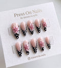 Stiletto-shaped black French tip press on nails with 3D pink flowers and white polka dots.