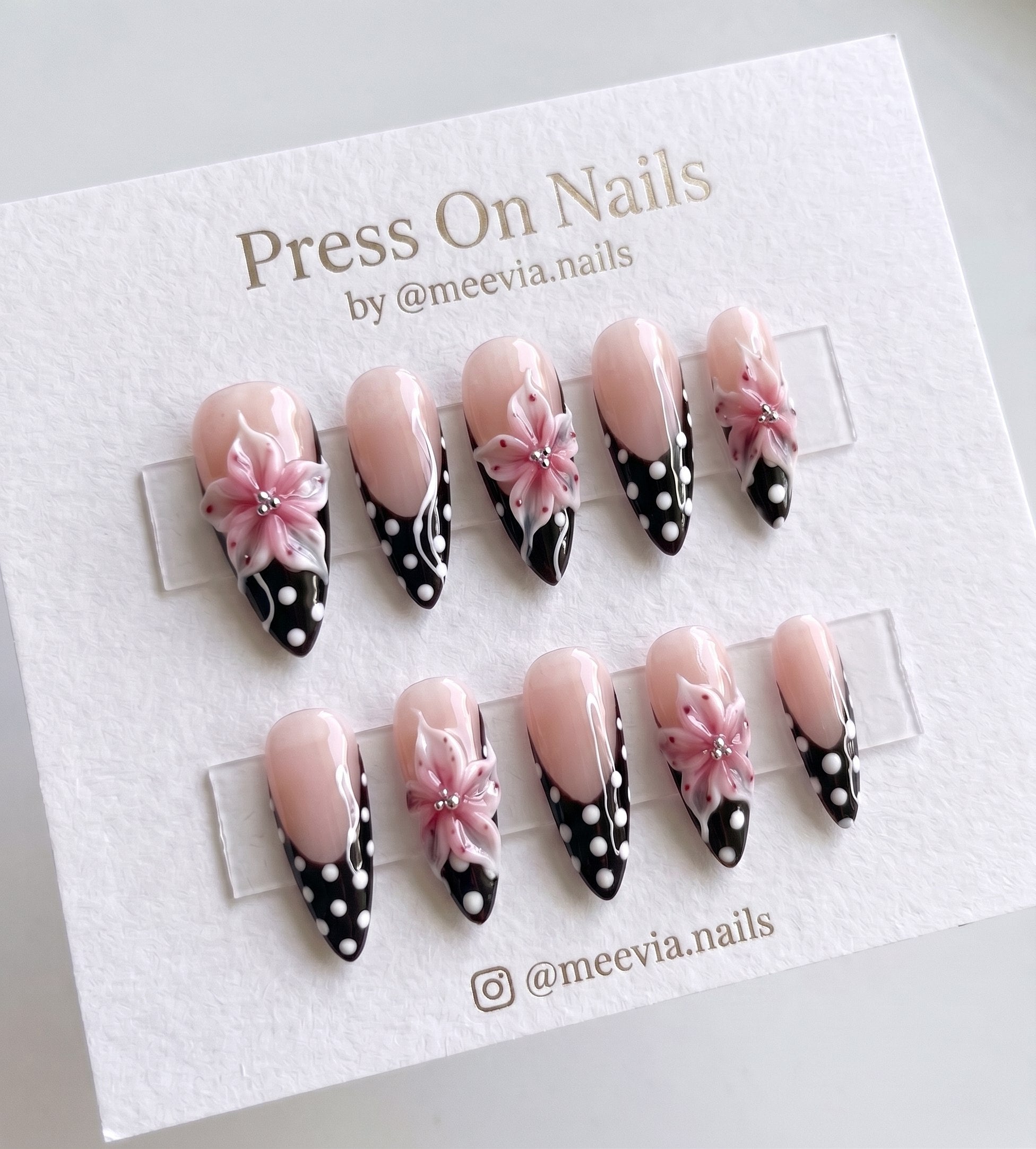 Stiletto-shaped black French tip press on nails with 3D pink flowers and white polka dots.
