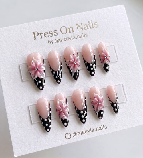 Stiletto-shaped black French tip press on nails with 3D pink flowers and white polka dots.
