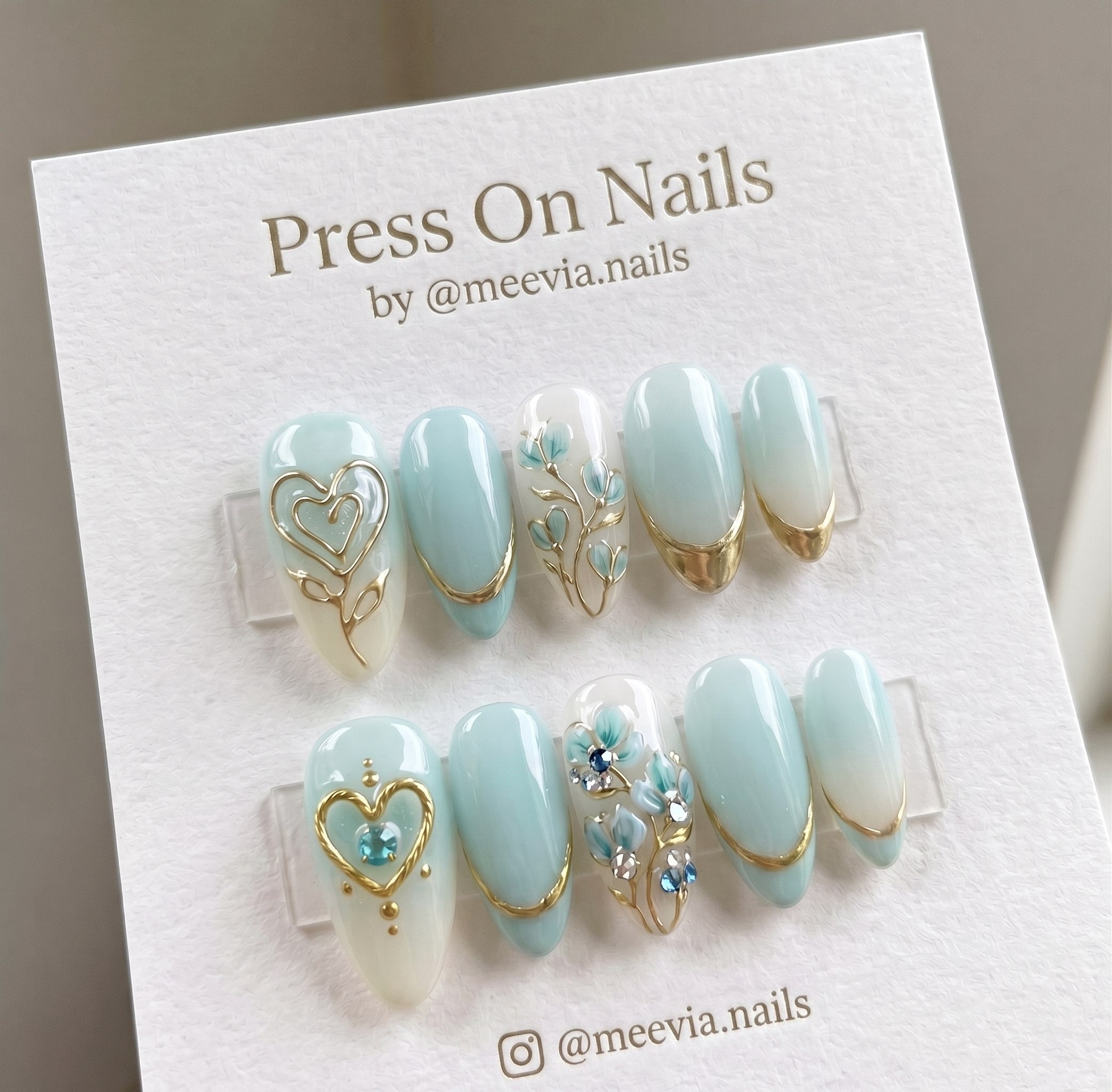 Almond-shaped light blue and white press-on nail set with 3D gold hearts and floral art