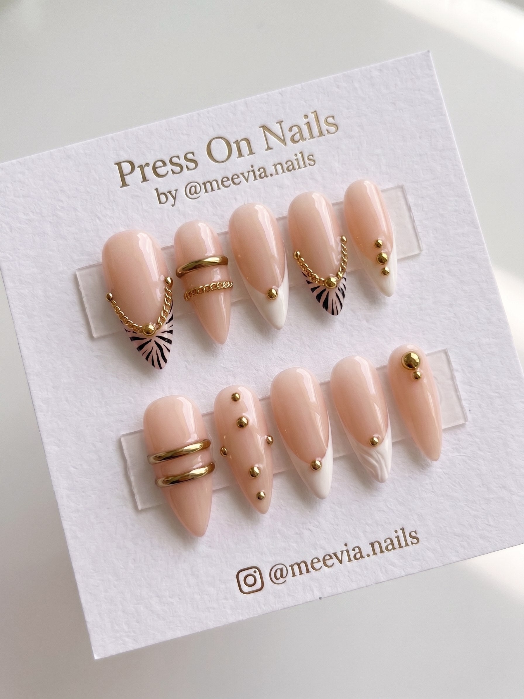 Stiletto-shaped nude press-on nails with gold chains and black animal print motifs