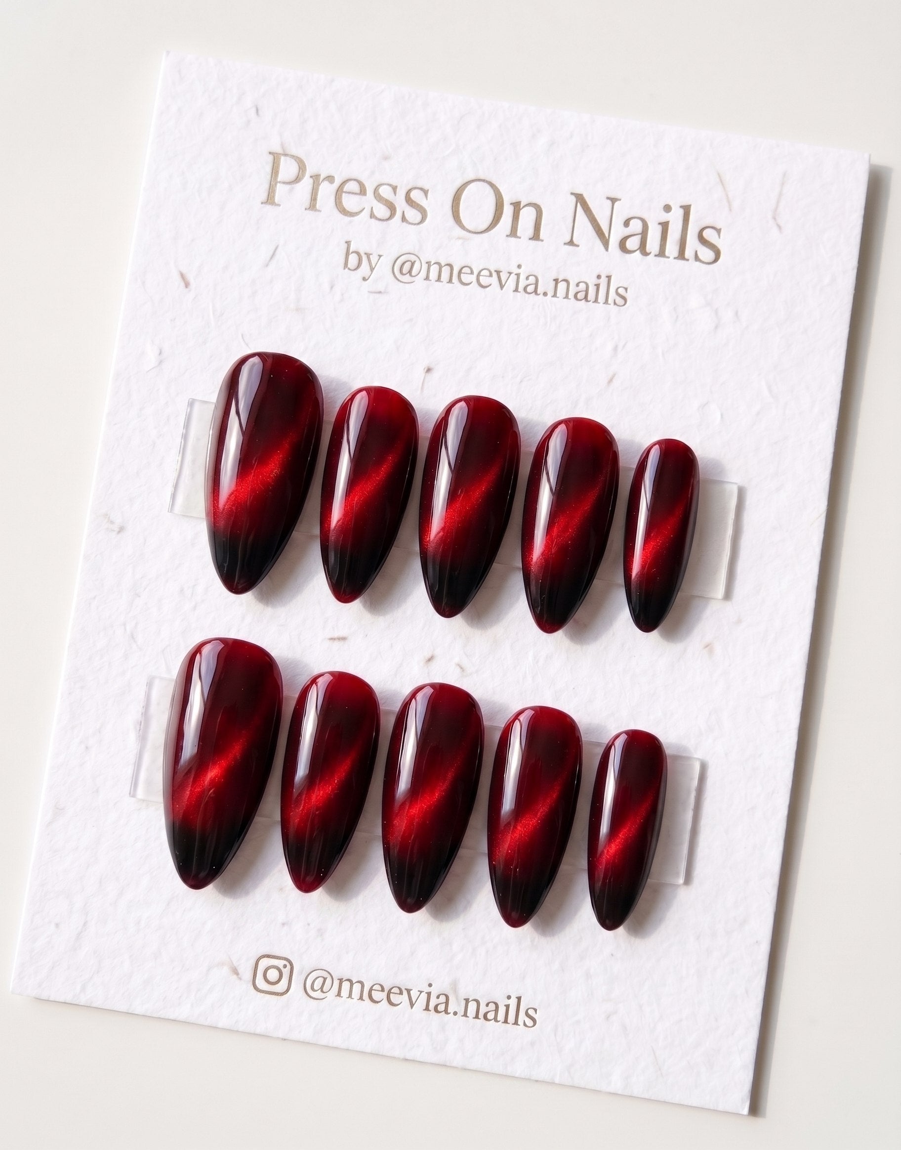 Almond-shaped red cat eye press-on nails with a magnetic shimmer finish