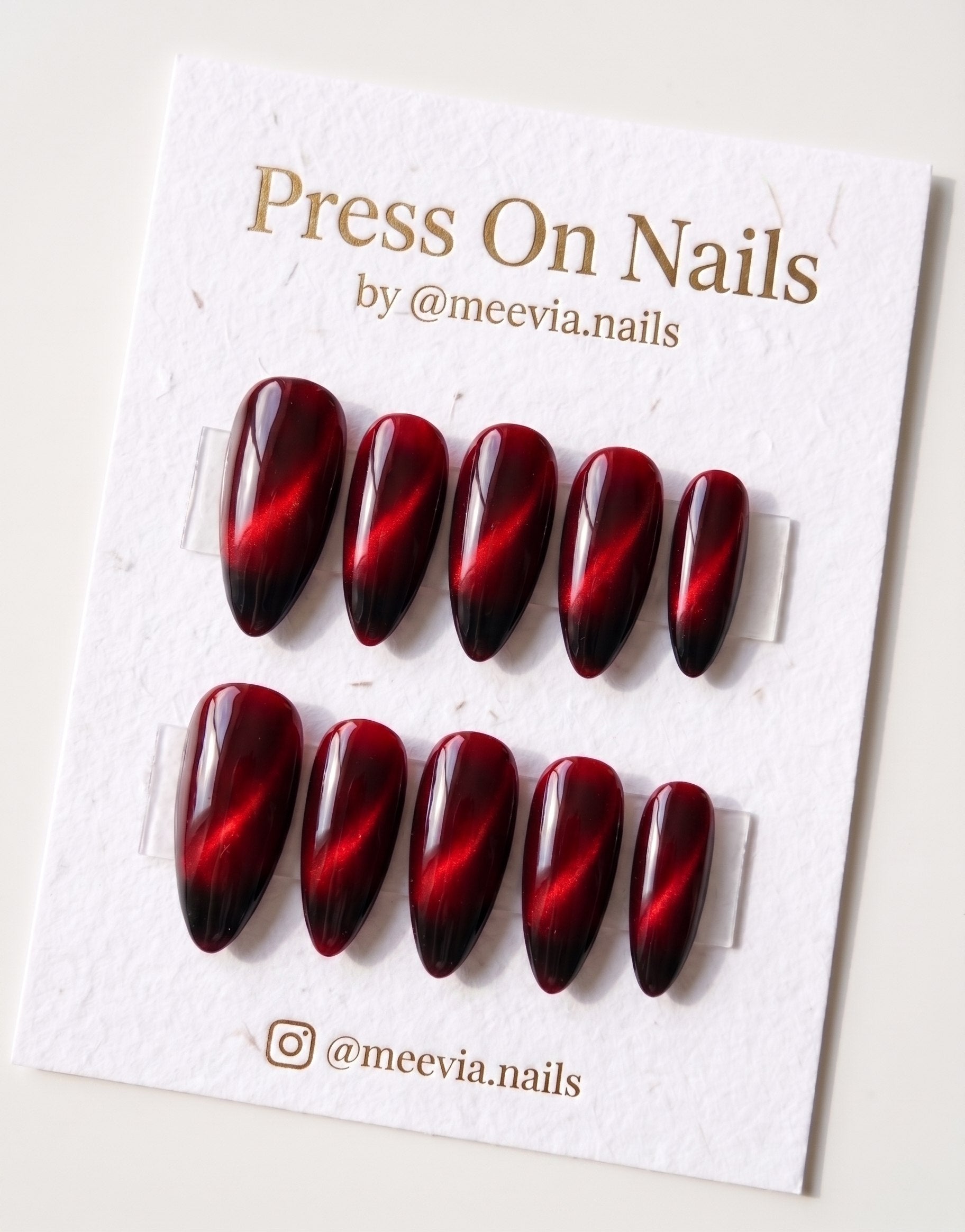 Almond-shaped deep red cat eye press-on nail set with magnetic shimmer and black ombre tips