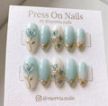 Almond-shaped mint blue and white press-on nails with 3D heart petals and gold metallic vine designs.