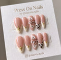 Almond-shaped nude press on nails with 3D white flowers, leopard print tips, and gold star charms.