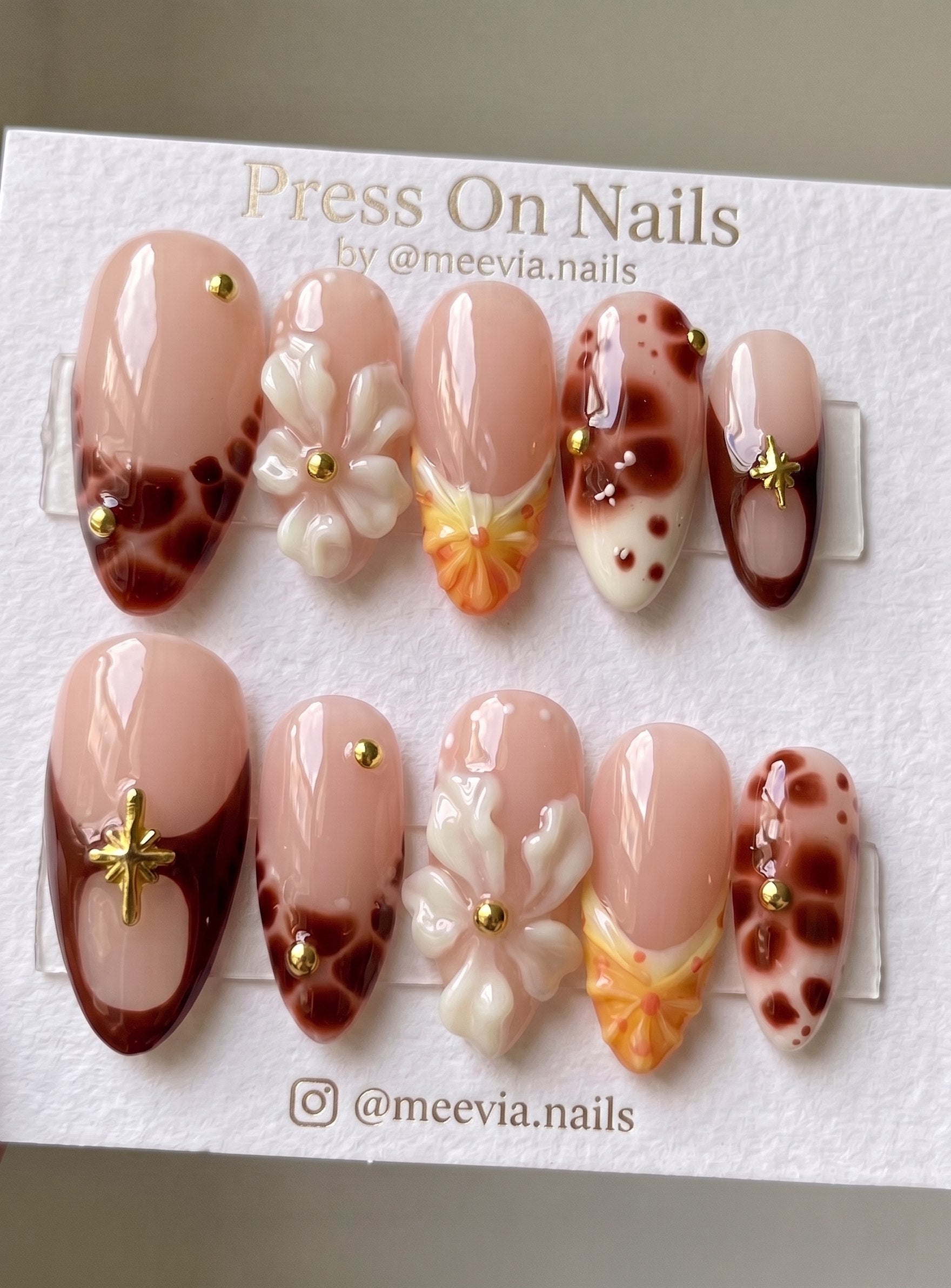 Almond-shaped nude press-on nails with 3D white flowers and brown tortoiseshell accents