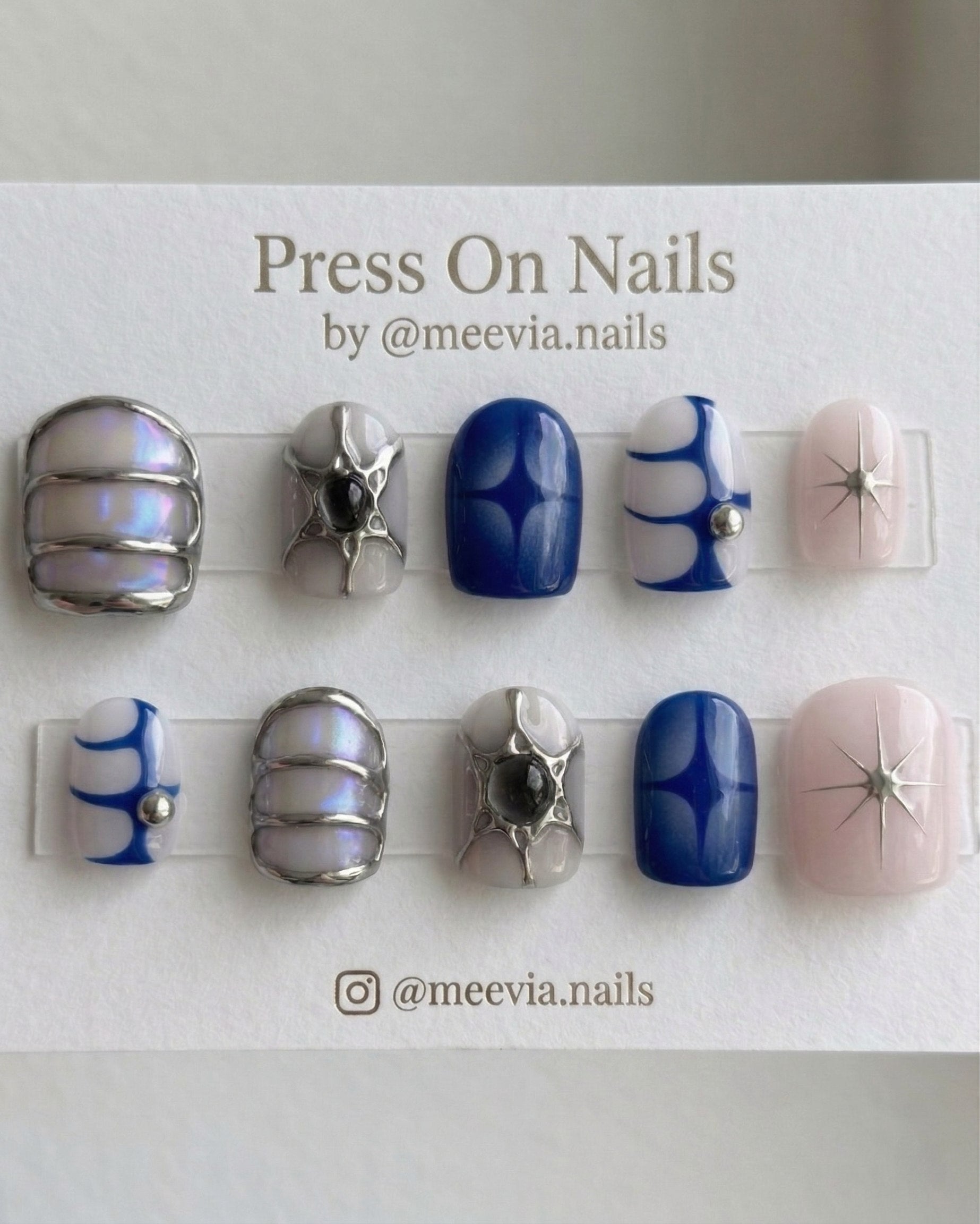 Short oval celestial press-on nail set with 3D silver accents, blue star motifs, and iridescent finishes