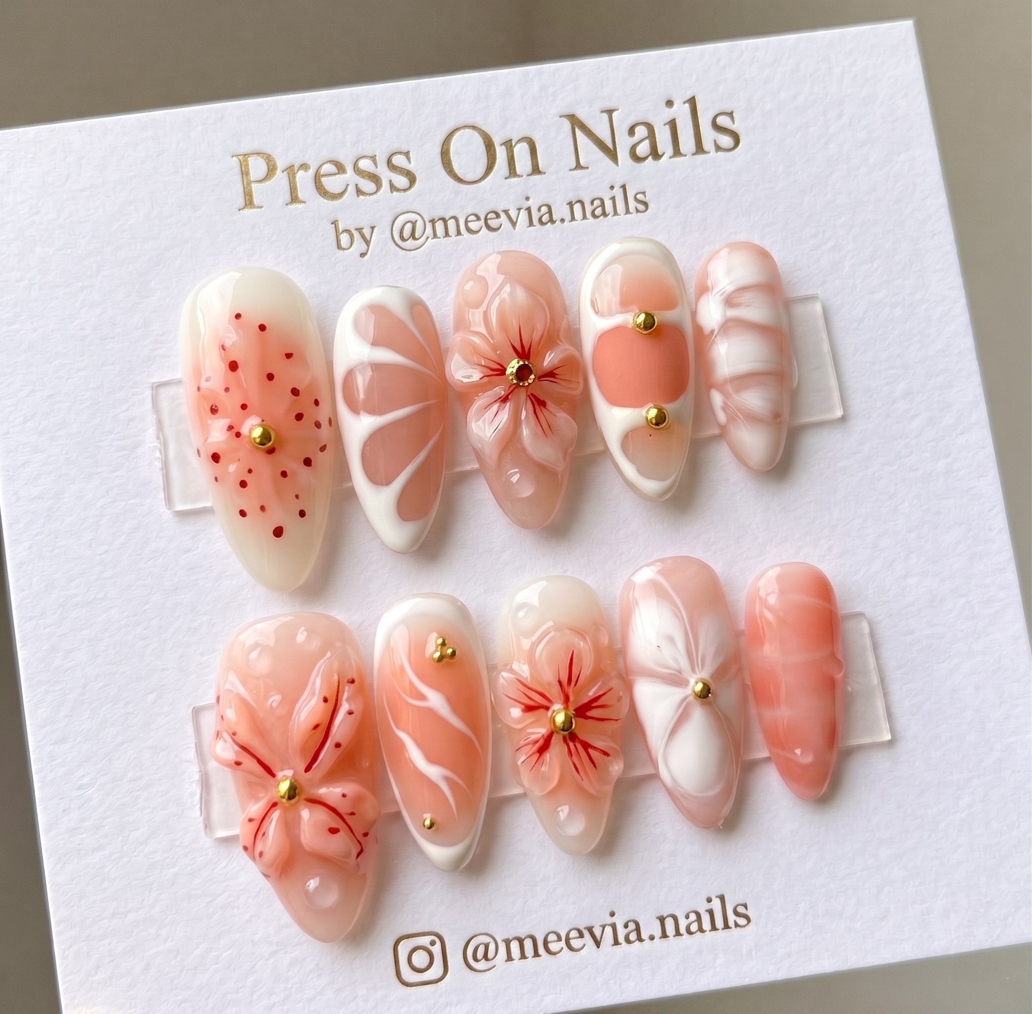 Almond-shaped peach and white press-on nail set with 3D floral designs and gold studs