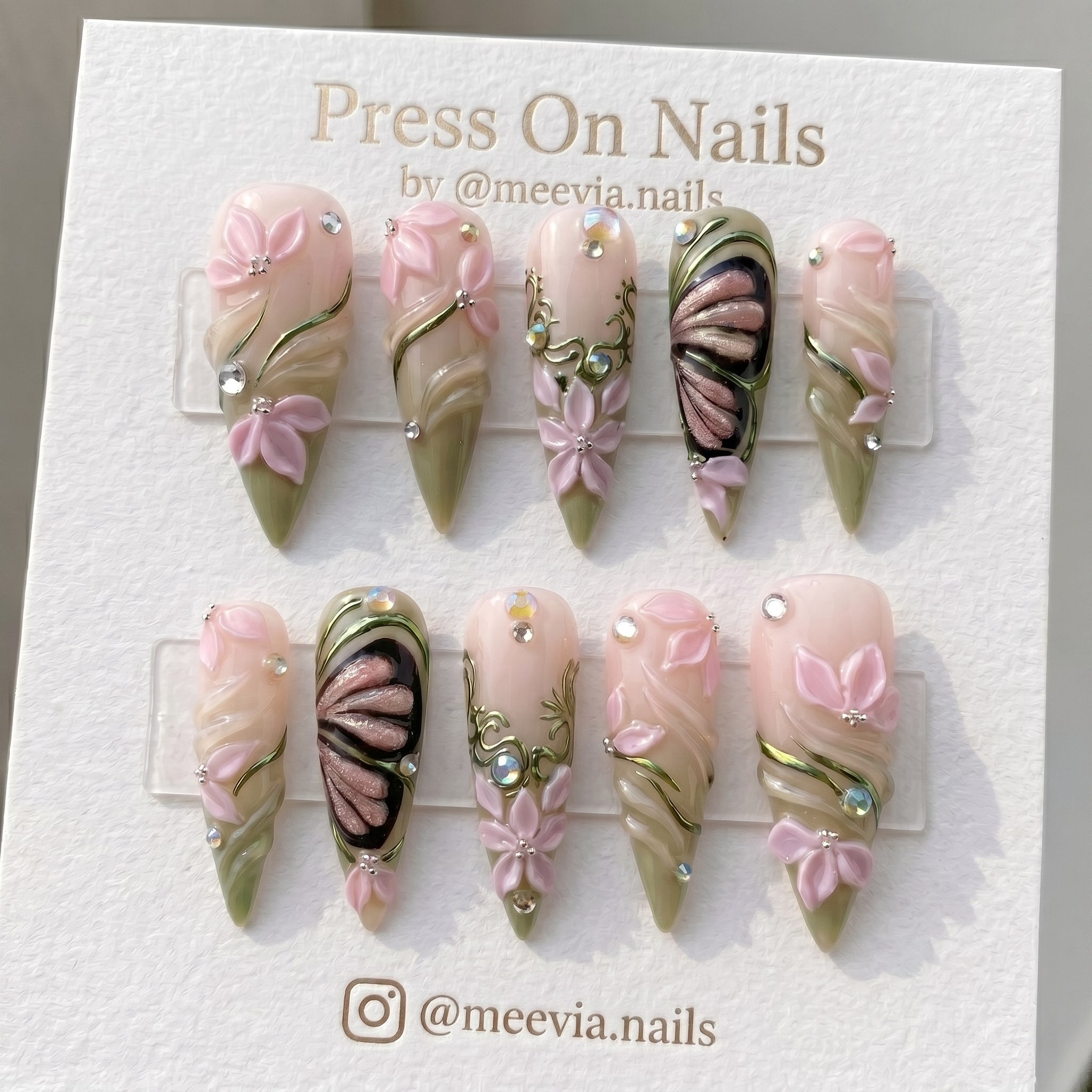 Stiletto-shaped pink and green press-on nails with 3D flowers and metallic butterfly art