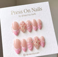Almond-shaped pink French tip press-on nails with 3D floral accents and gems