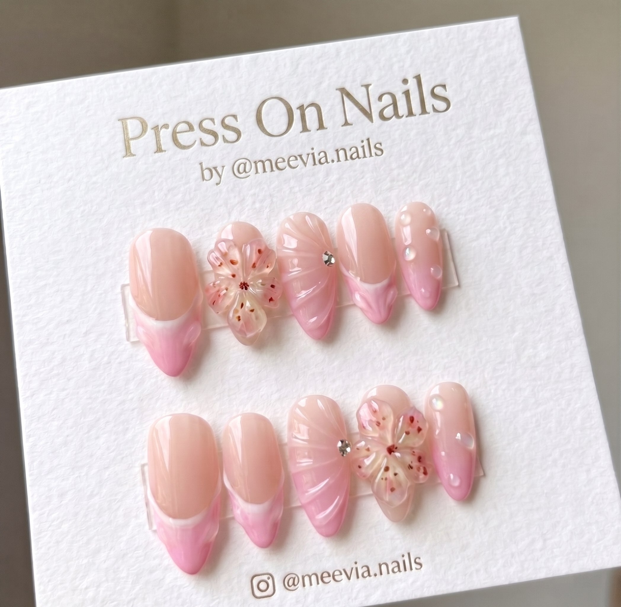 Almond-shaped pink French tip press-on nails with 3D floral accents and gems