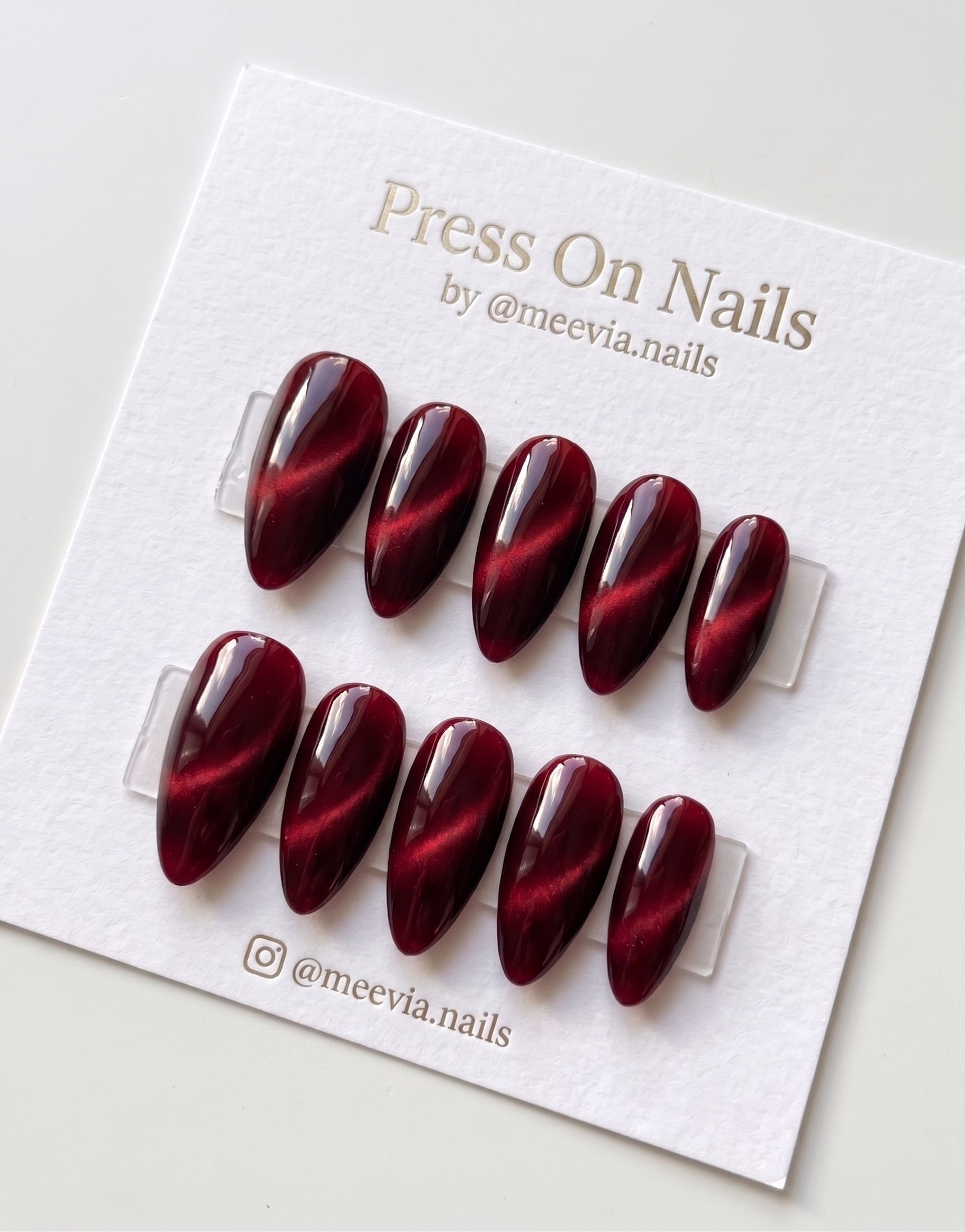 Almond-shaped burgundy cat eye press on nails with a glossy velvet shimmer finish