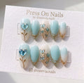 Oval-shaped blue and cream press-on nails with 3D gold floral vines and glass heart accents