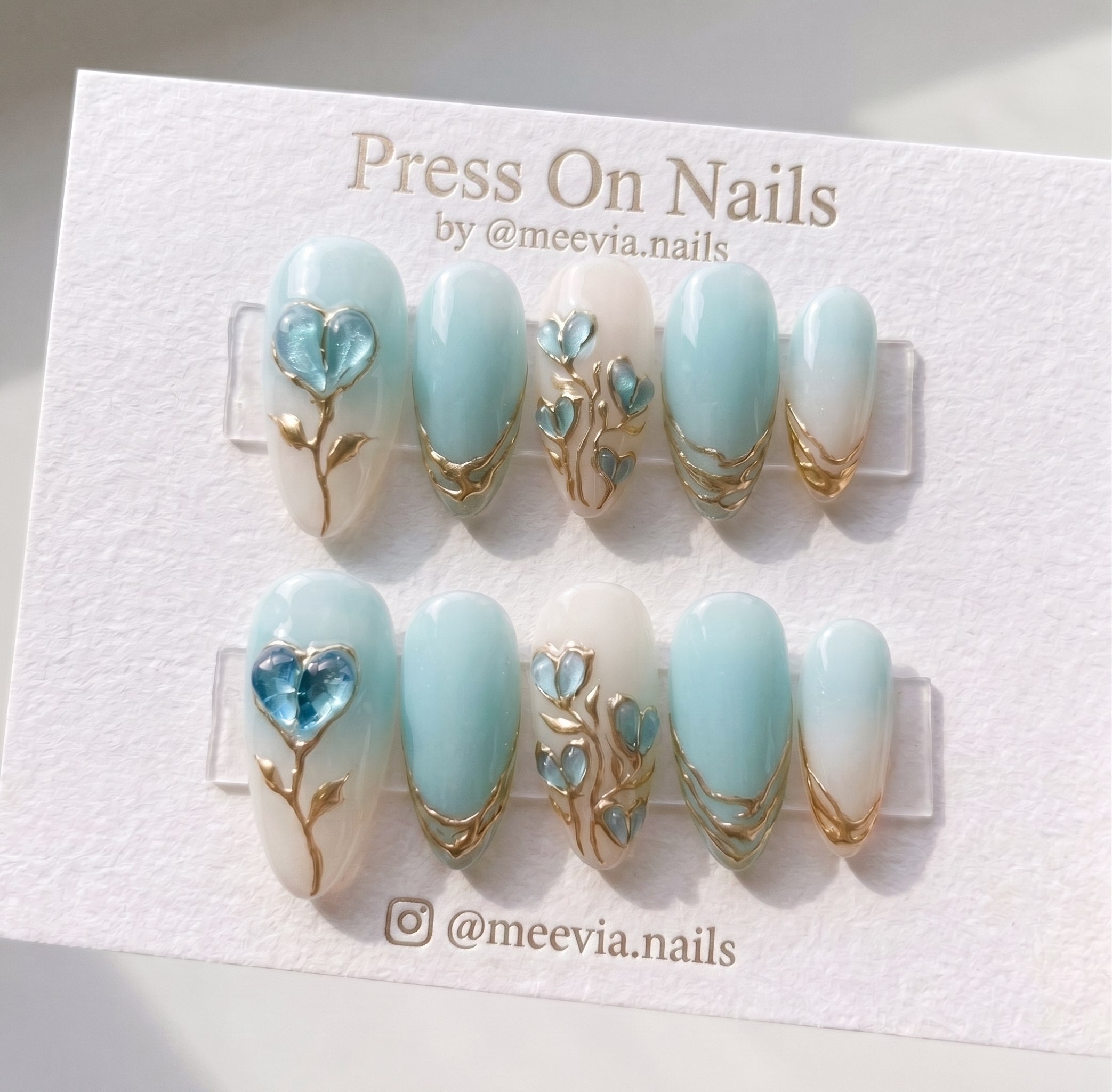 Oval-shaped blue and cream press-on nails with 3D gold floral vines and glass heart accents