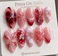 Almond-shaped pink and red press-on nails featuring 3D floral art and nautical charms