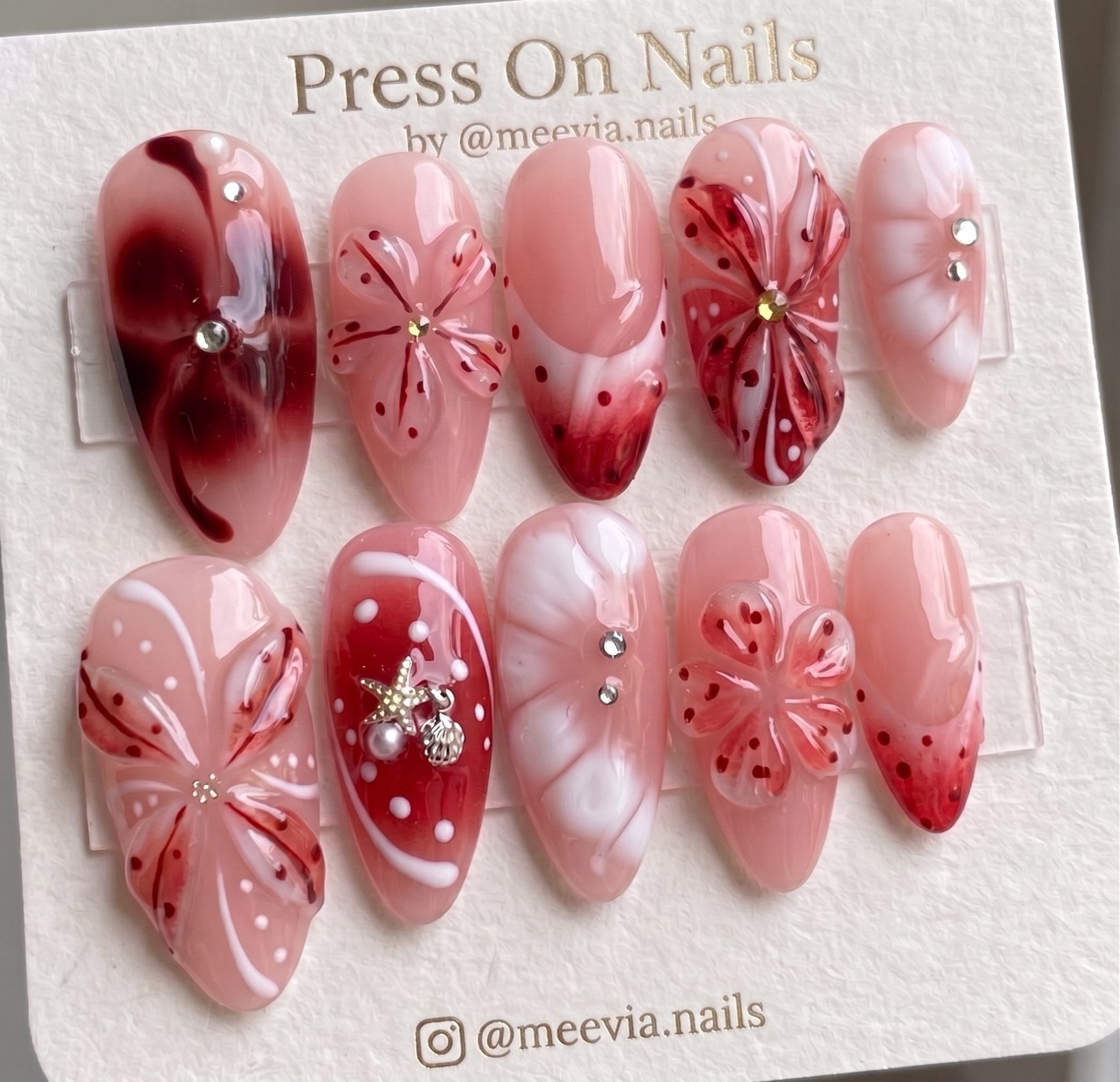 Almond-shaped pink and red press-on nails featuring 3D floral art and nautical charms