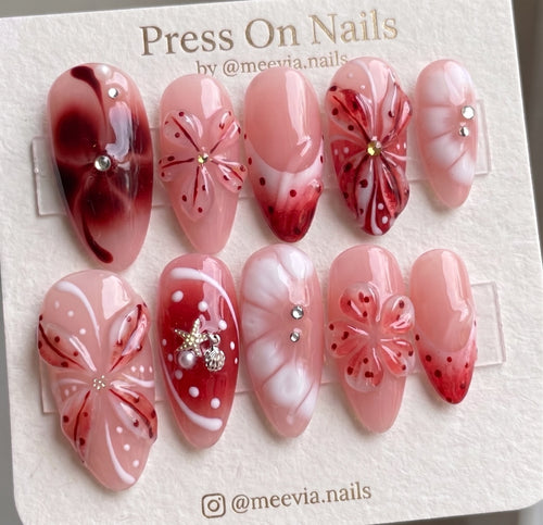 Almond-shaped pink and red press-on nails featuring 3D floral art and nautical charms