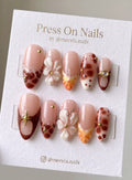Almond-shaped press-on nails with brown tortoise patterns, 3D white flowers, and gold charms.