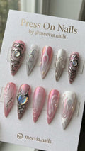 Long stiletto-shaped pink press-on nails with silver 3D chrome accents and iridescent heart gems.