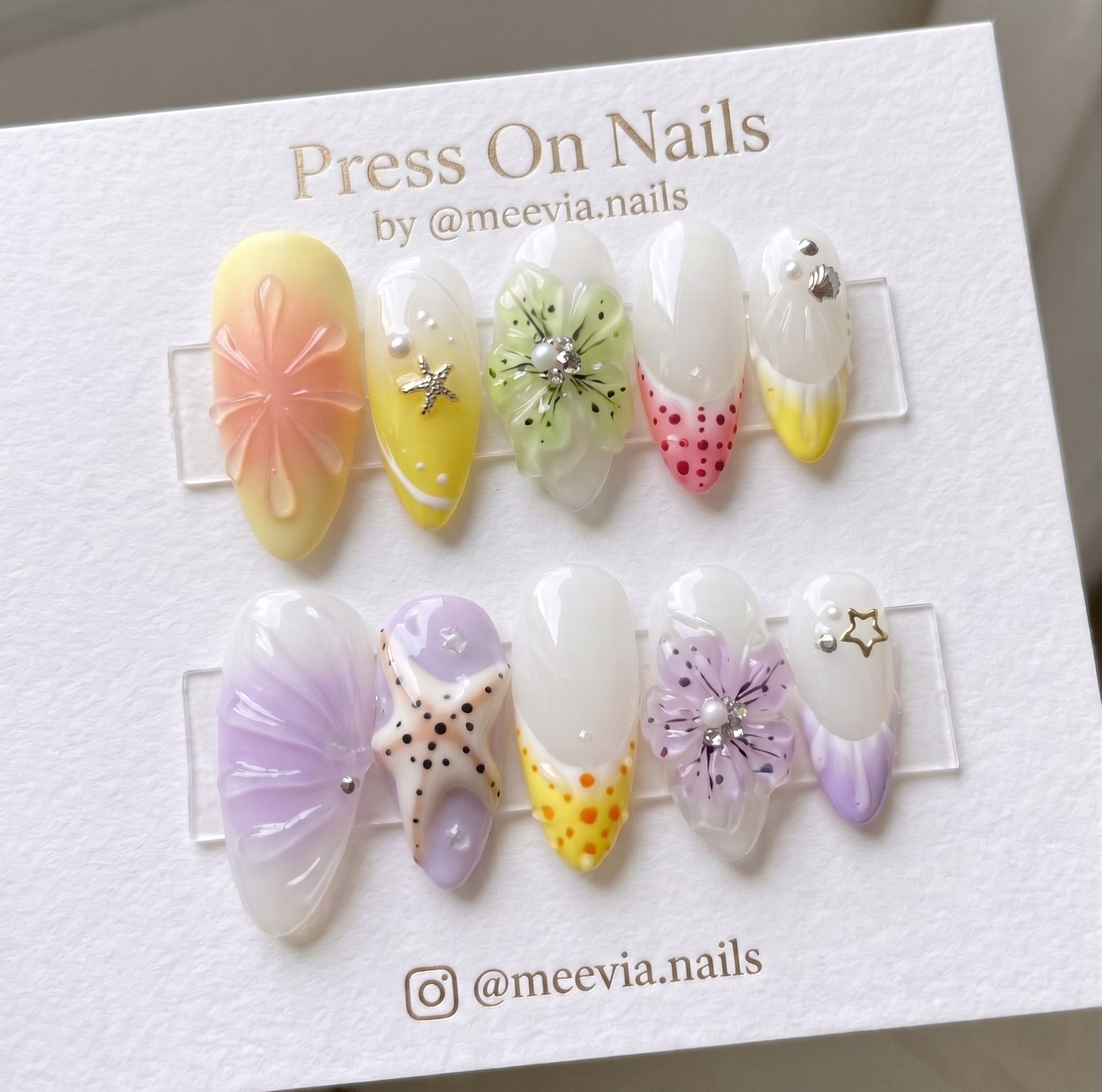 Almond-shaped press-on nails featuring 3D floral and starfish nail art in yellow and purple tones.