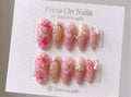 Almond-shaped pink press-on nails with 3D floral art, pearls, and butterfly accents