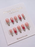 Stiletto-shaped French tip press-on nails with polka dots and pink 3D floral accents.