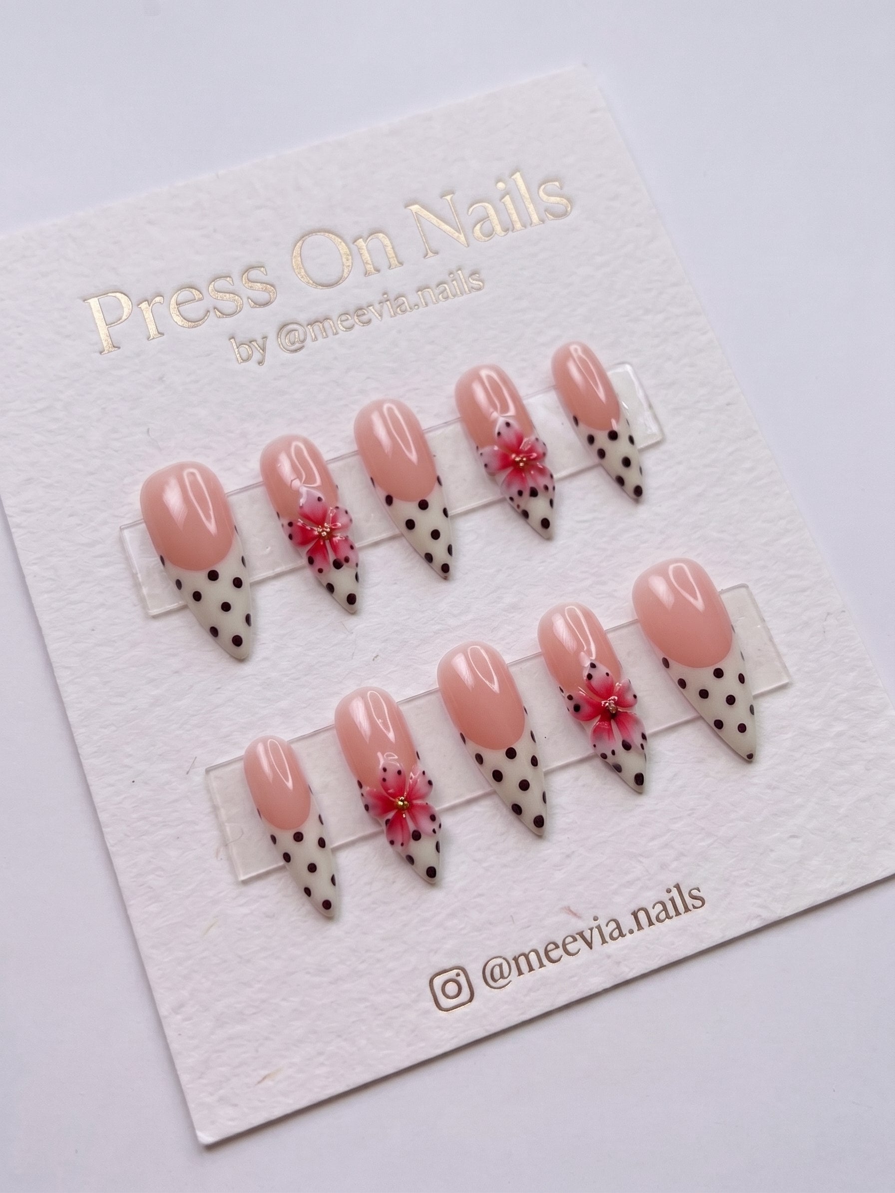 Stiletto-shaped French tip press-on nails with polka dots and pink 3D floral accents.