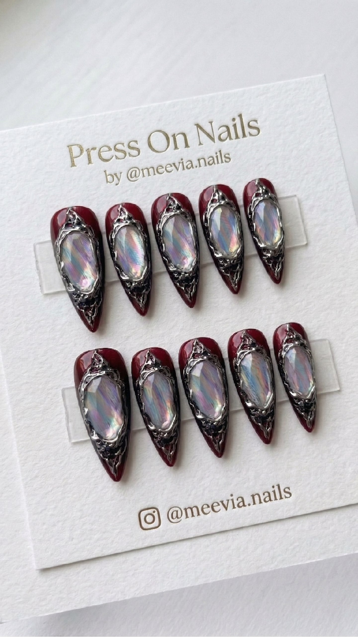 Stiletto-shaped deep red press on nails with ornate 3D silver frames and iridescent stones