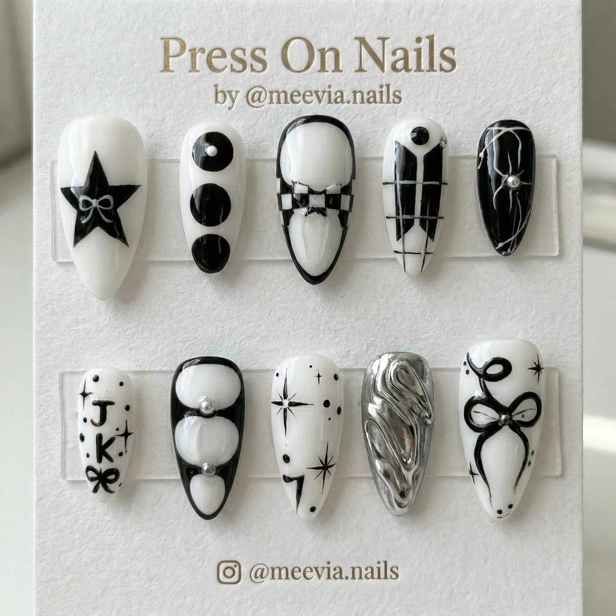 Stiletto-shaped black and white press-on nail set with stars, bows, and 3D silver chrome accents.