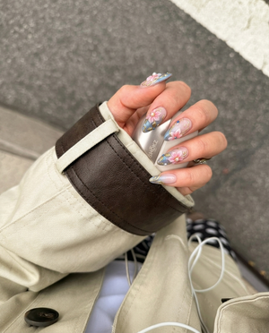 Pink and grey gradient press-on nails featuring 3D floral art, gold metallic swirls, pearls, and blue rhinestones.
