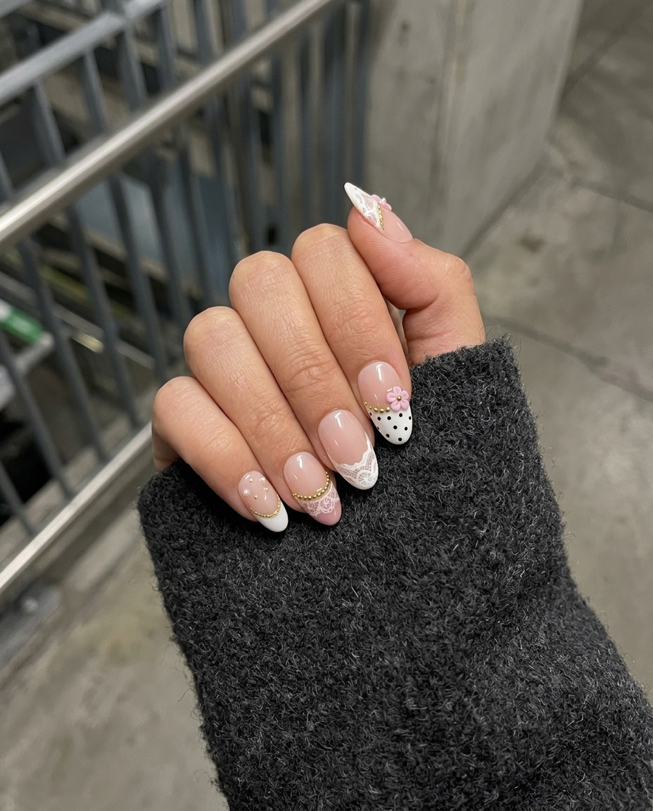 A set of press-on nails with white lace patterns, black polka dots, 3D pink flowers, gold beads, and pearl embellishments.