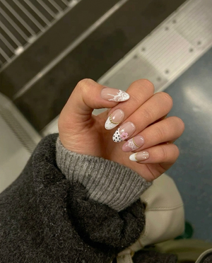 A set of press-on nails with white lace patterns, black polka dots, 3D pink flowers, gold beads, and pearl embellishments.