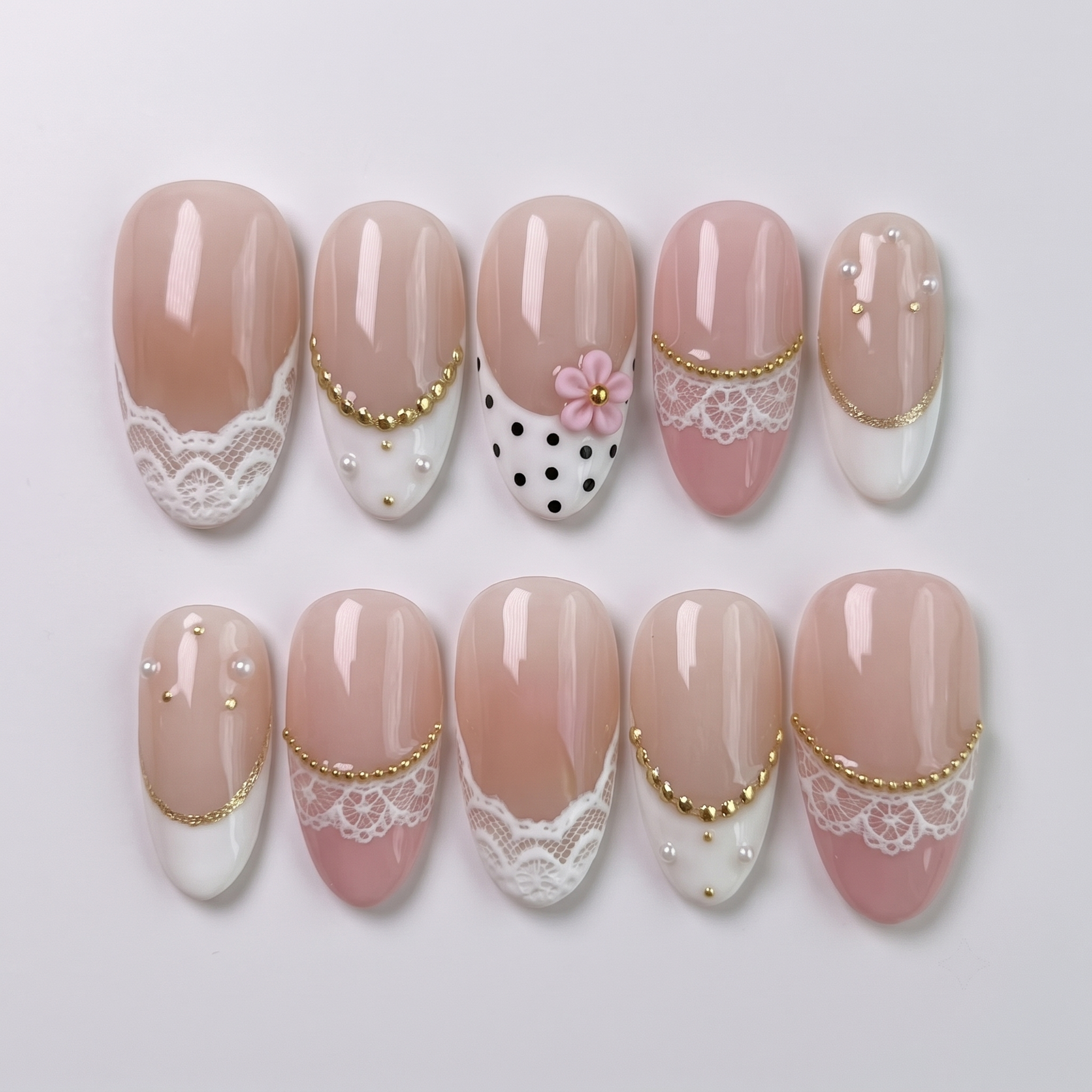 A set of press-on nails with white lace patterns, black polka dots, 3D pink flowers, gold beads, and pearl embellishments.