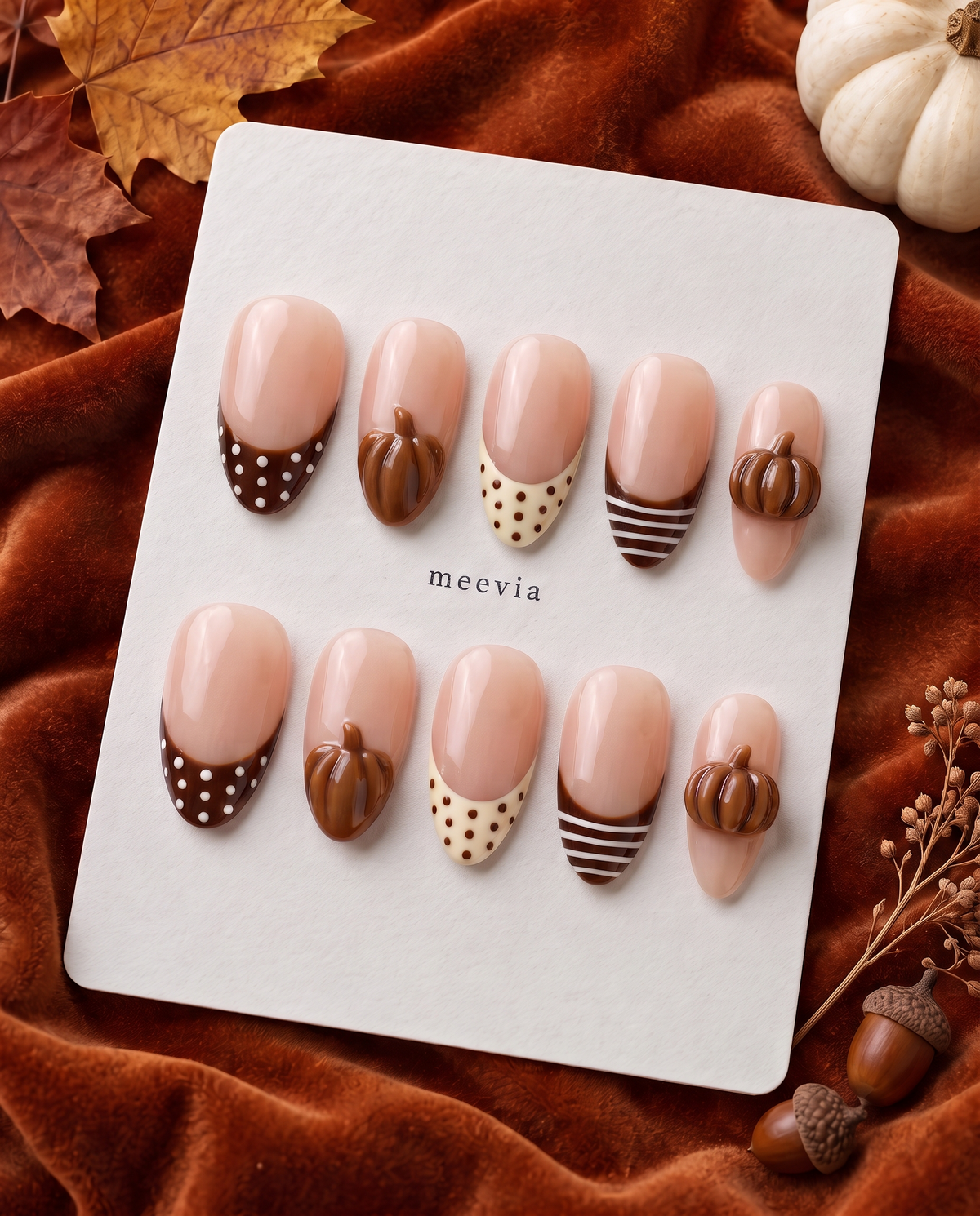 Glossy nude press-on nails with brown French tips, polka dots, stripes, and raised pumpkin accents
