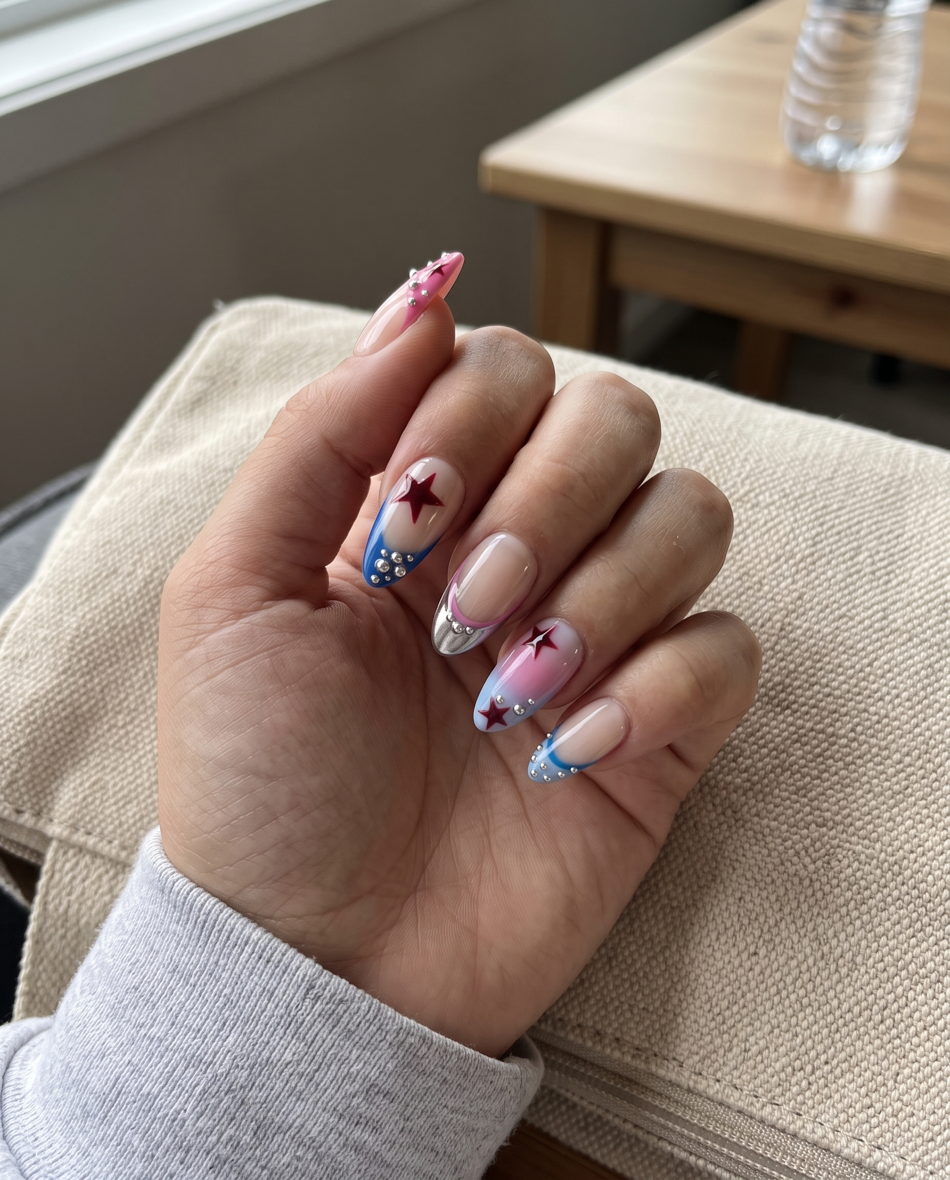 A set of press-on nails featuring a French tip design with red star accents and silver beads on a nude base.