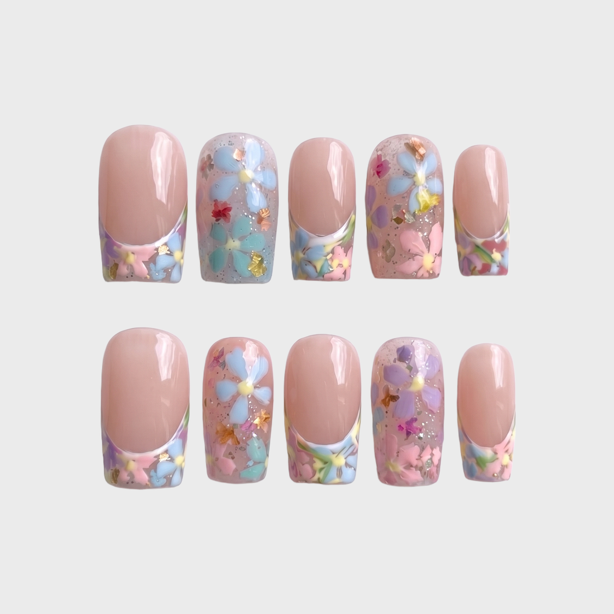 A set of press-on nails featuring a French tip design with floral motifs, gold foil, and glitter on a sheer base.