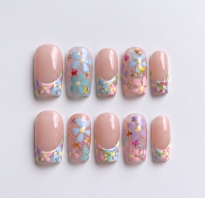 A set of press-on nails featuring a French tip design with floral motifs, gold foil, and glitter on a sheer base.