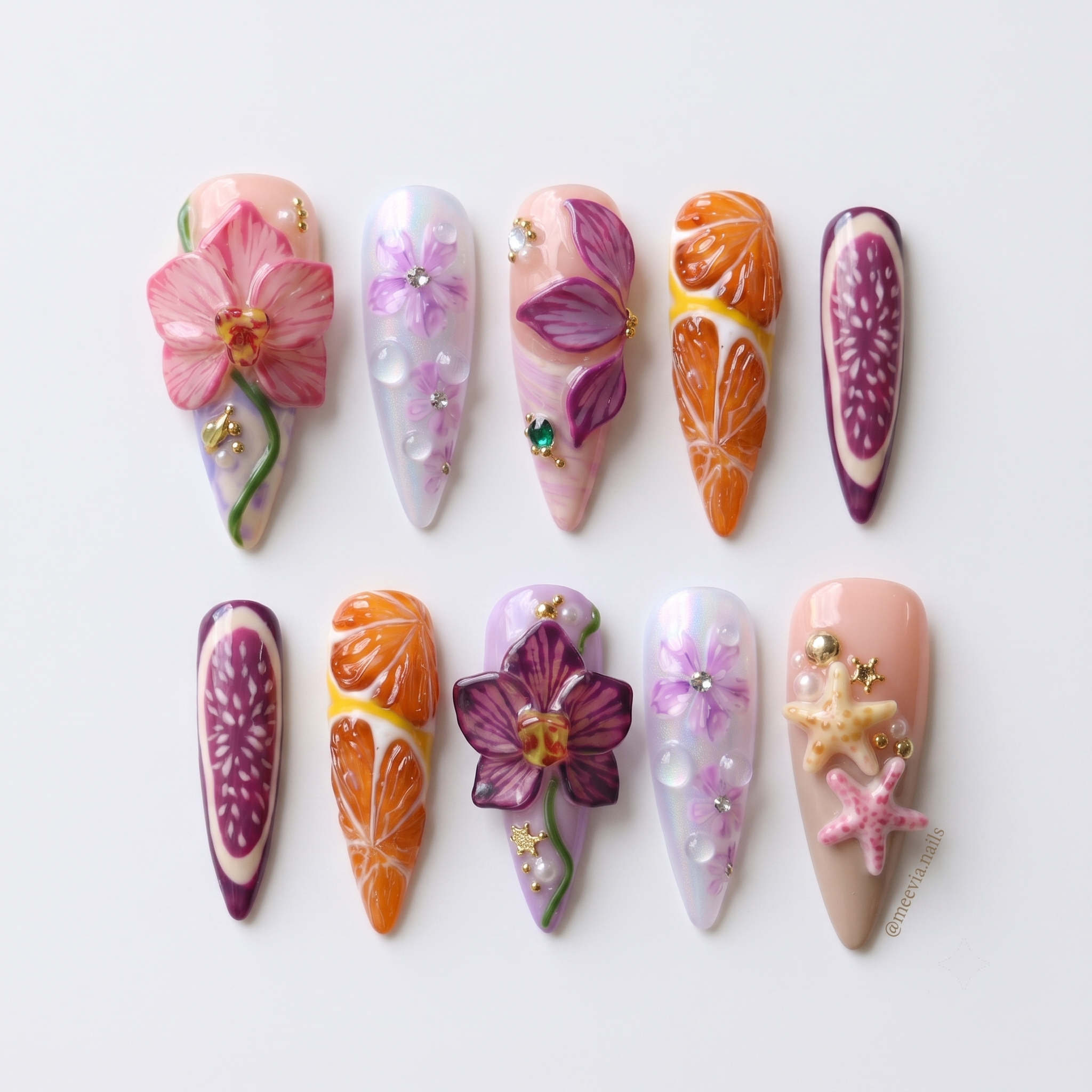 A set of stiletto-shaped press-on nails featuring 3D orchids, orange slices, fig patterns, and starfish embellishments.