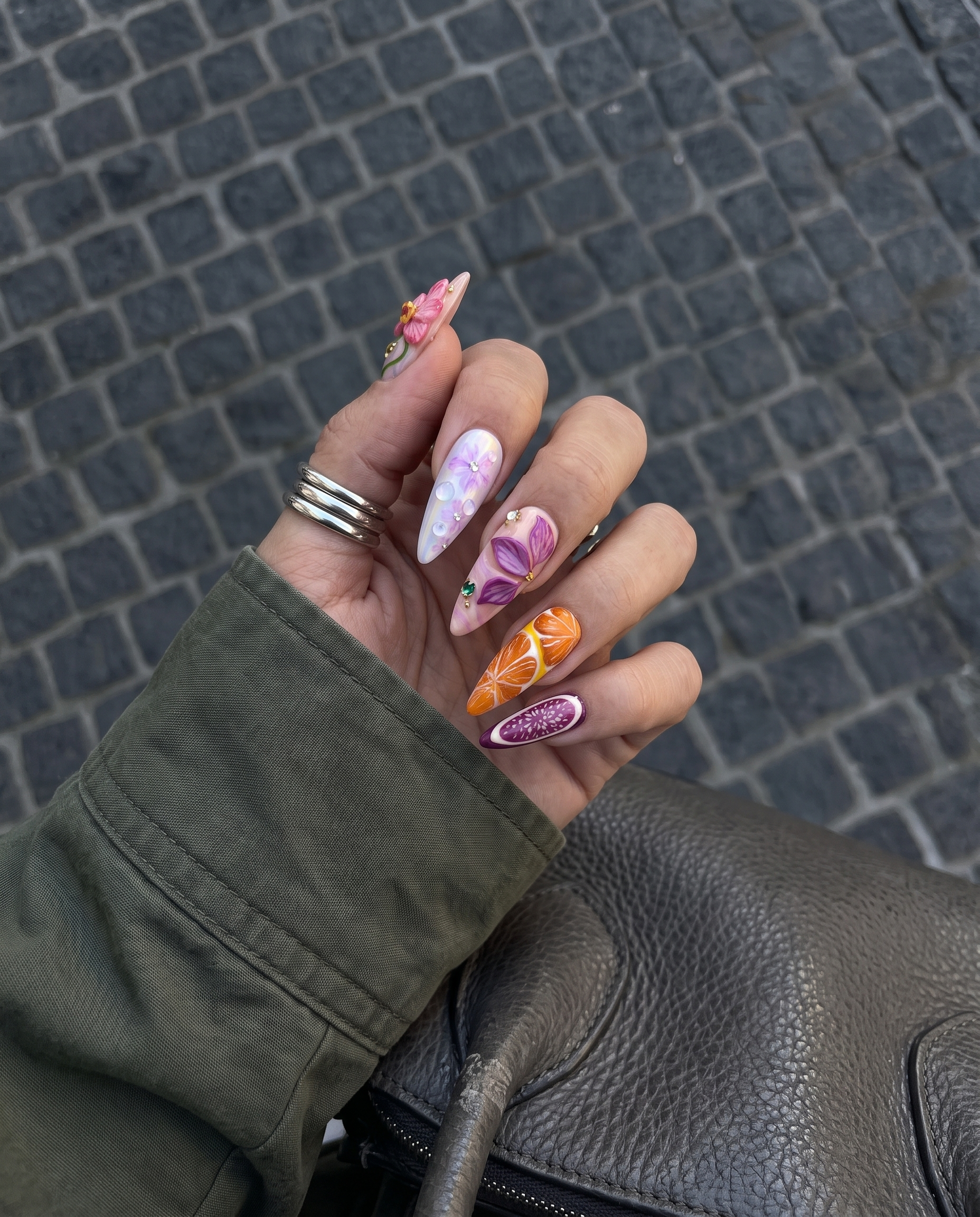 A set of stiletto-shaped press-on nails featuring 3D orchids, orange slices, fig patterns, and starfish embellishments.