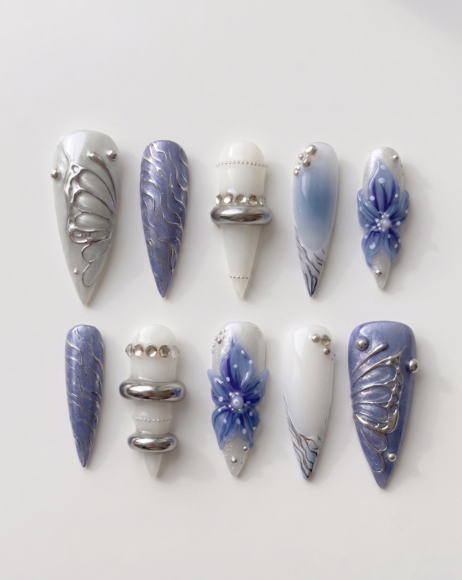 A set of press-on nails featuring blue floral designs, 3D silver chrome butterfly wings, and metallic ring accents.