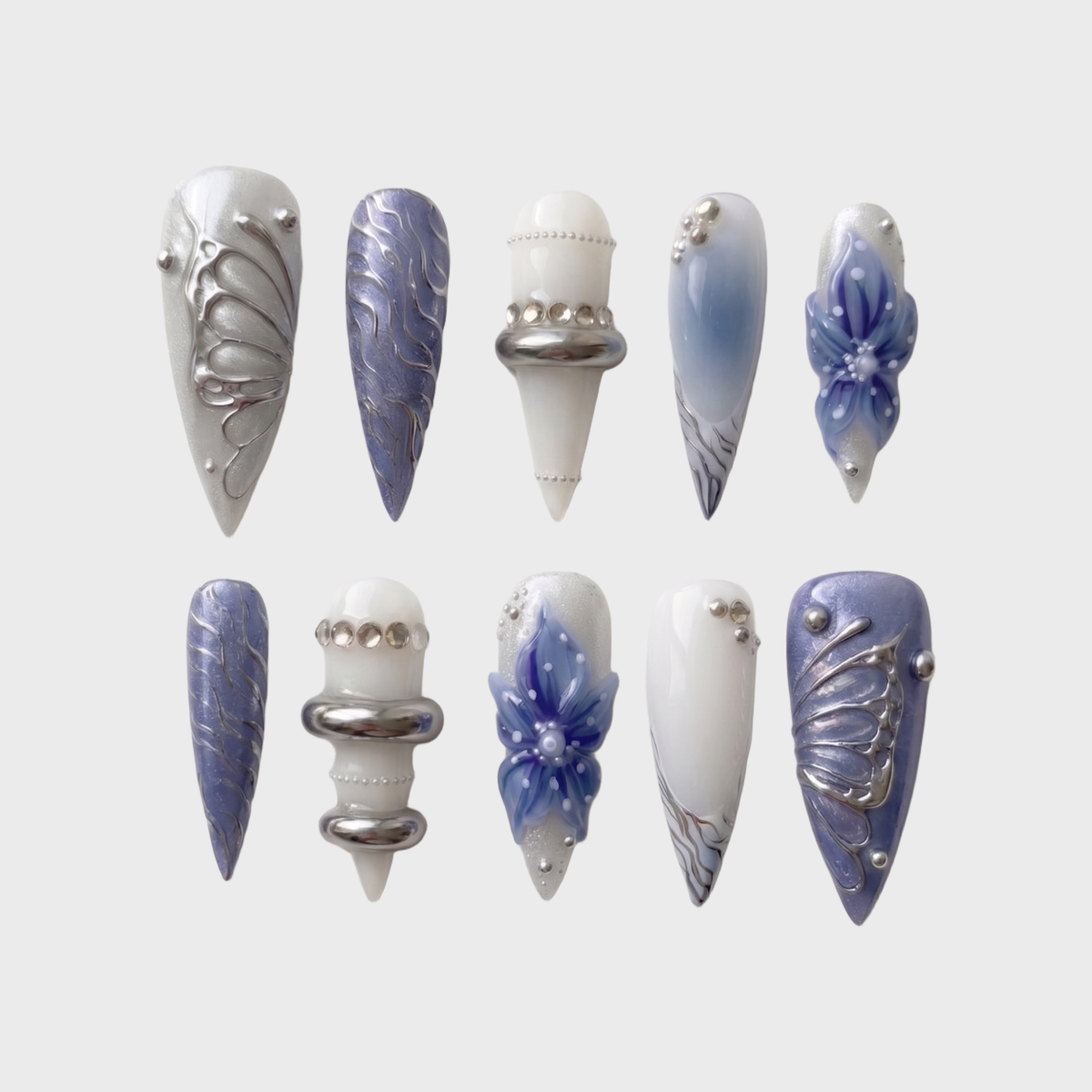 A set of press-on nails featuring blue floral designs, 3D silver chrome butterfly wings, and metallic ring accents.