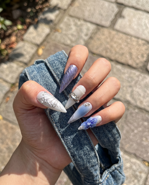 A set of press-on nails featuring blue floral designs, 3D silver chrome butterfly wings, and metallic ring accents.