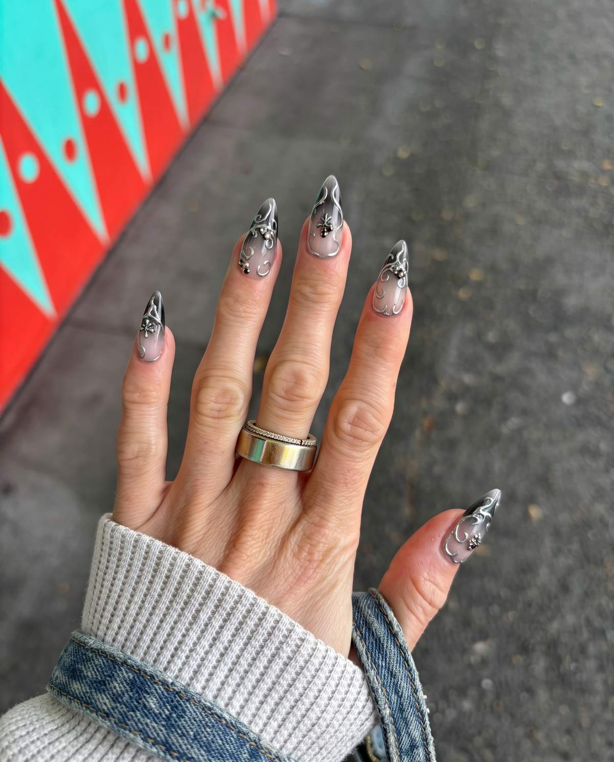 A set of stiletto press-on nails with a dark grey ombre gradient and silver filigree embellishments.